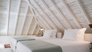 Une chambre avec un plafond en pente, un lit recouvert de linge de lit blanc, une table de chevet avec une lampe et un petit tapis sur le sol.