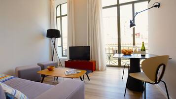 Een moderne woonkamer met een bank, een salontafel, een televisie en een eethoek met een tafel en stoelen.