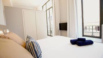 Habitación de hotel con cama, almohadas, televisor y ventana con cortinas.
