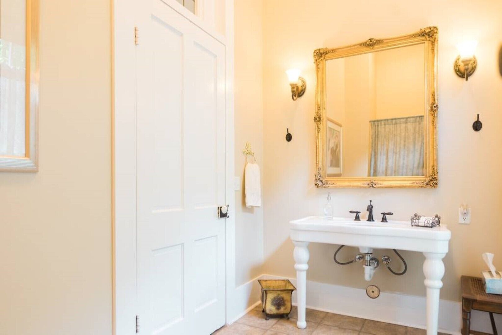 Un baño con un lavamanos blanco, un espejo con marco dorado y una puerta blanca.