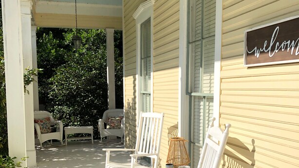 A porch with white rocking chairs and a wicker table, a welcome sign, and a hanging lantern. - Lovely Historic Home Downtown Columbus  (Columbus)