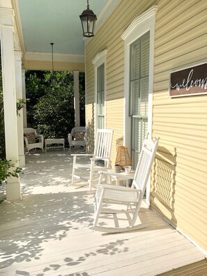 A porch with white rocking chairs and a wicker table, a welcome sign, and a hanging lantern. - Lovely Historic Home Downtown Columbus  (Columbus)