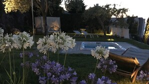 Un jardin avec une piscine, entouré de fleurs blanches et violettes, et un banc.