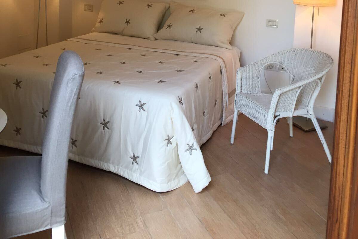 Ein Schlafzimmer mit einem Bett, zwei Nachttischlampen, einem Sessel und einem Bild an der Wand.