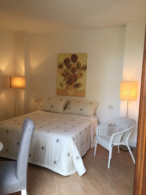 Un dormitorio con una cama, dos lámparas de noche, una silla y un cuadro en la pared.