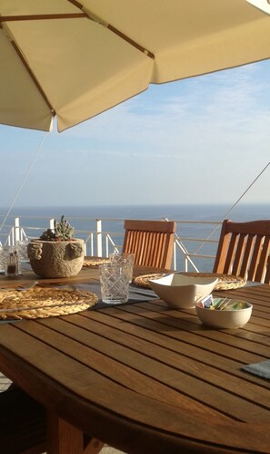 Een houten tafel met uitzicht op zee, een stenen pot en een kom.