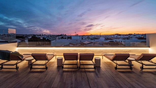 Eine Dachterrasse mit Liegestühlen und Blick auf die Skyline im Abendlicht.