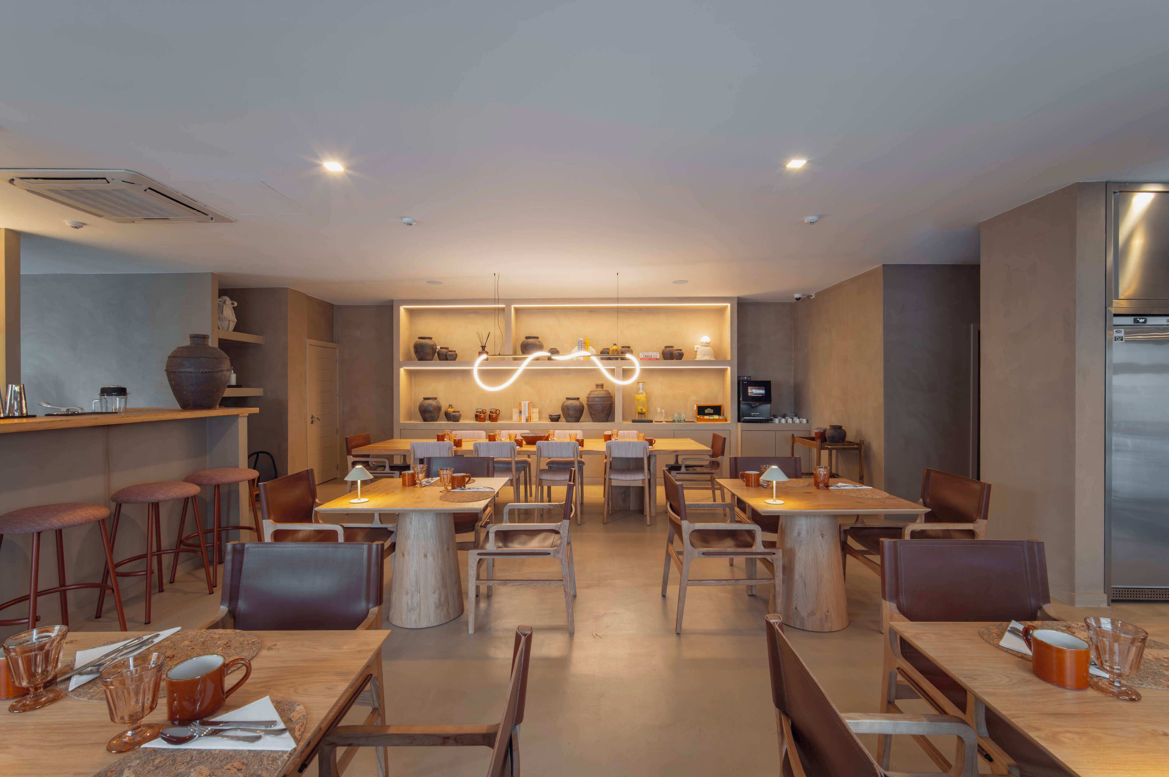 Ein modernes Restaurant mit Holztischen und -stühlen, einer zentralen Lichtinstallation und Regalen mit Dekorationen.