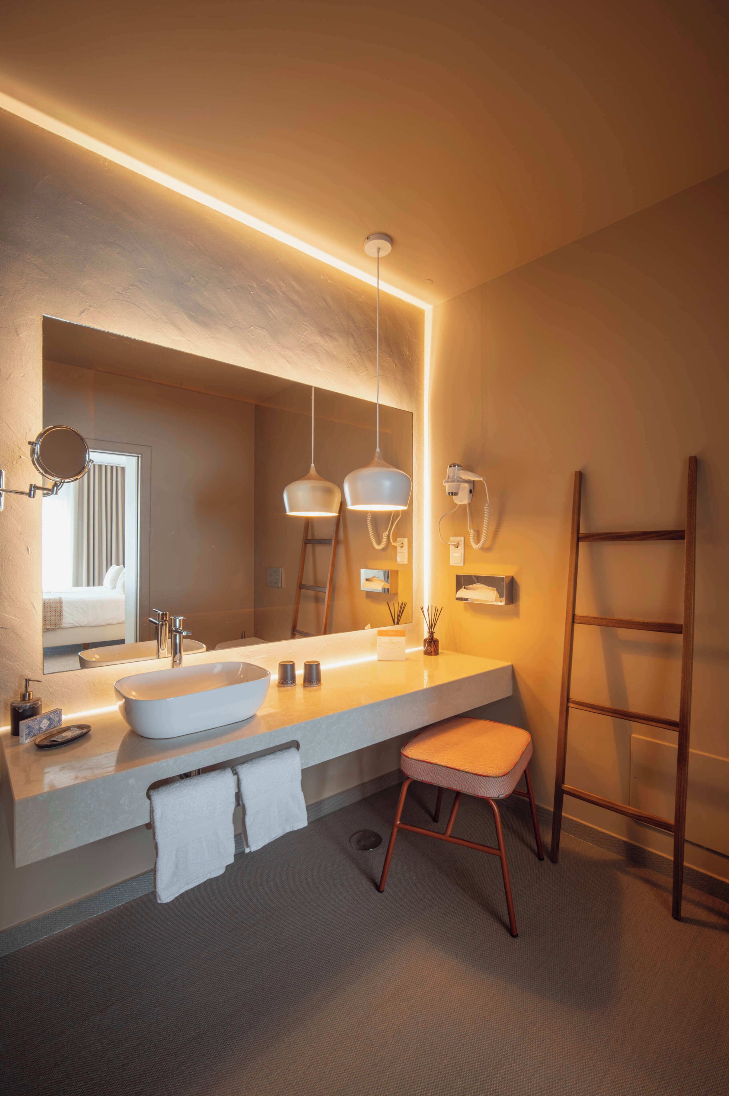 A modern bathroom with a large mirror, a vessel sink, and a wooden ladder.