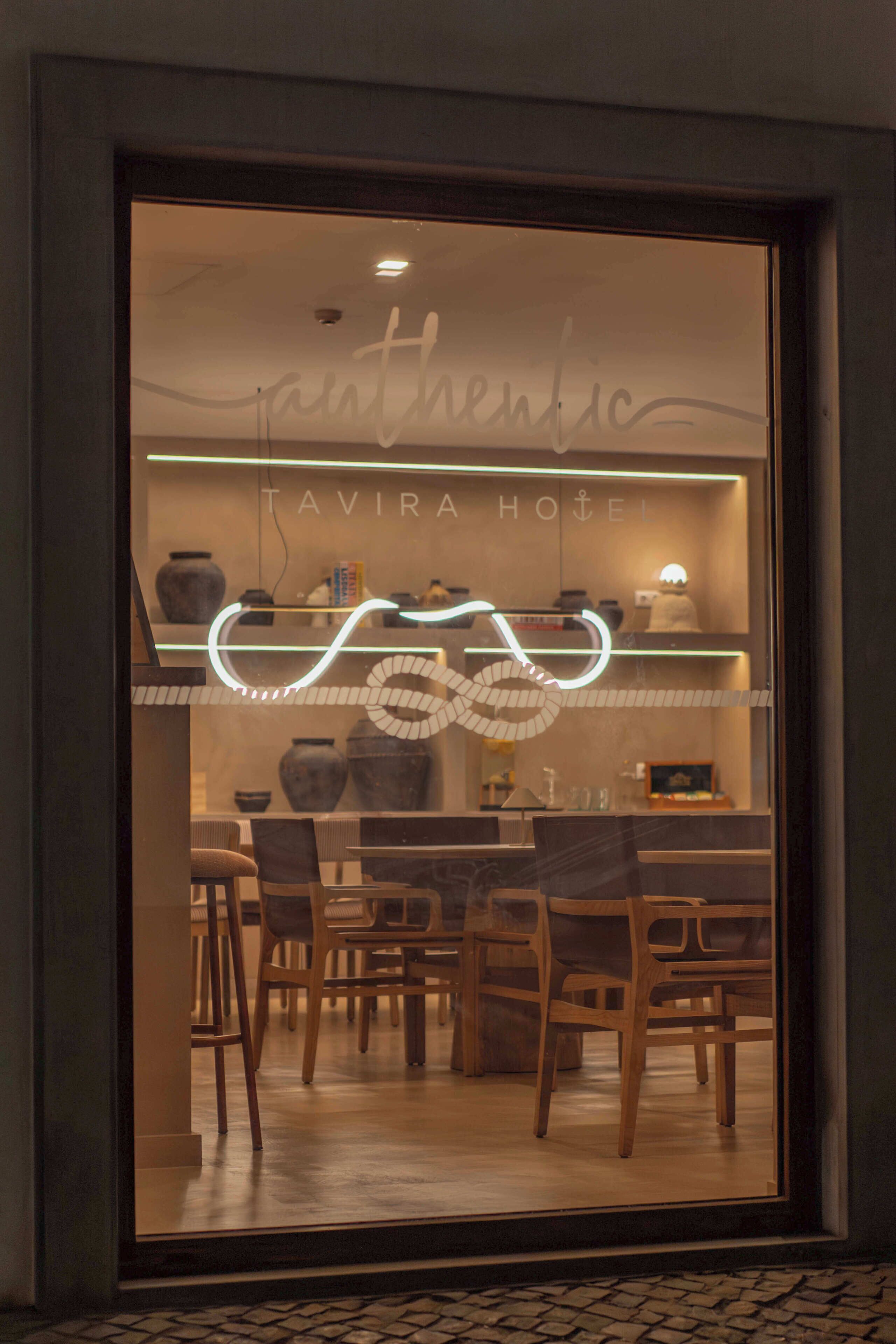 A restaurant with a neon sign, wooden chairs, and a tiled floor.