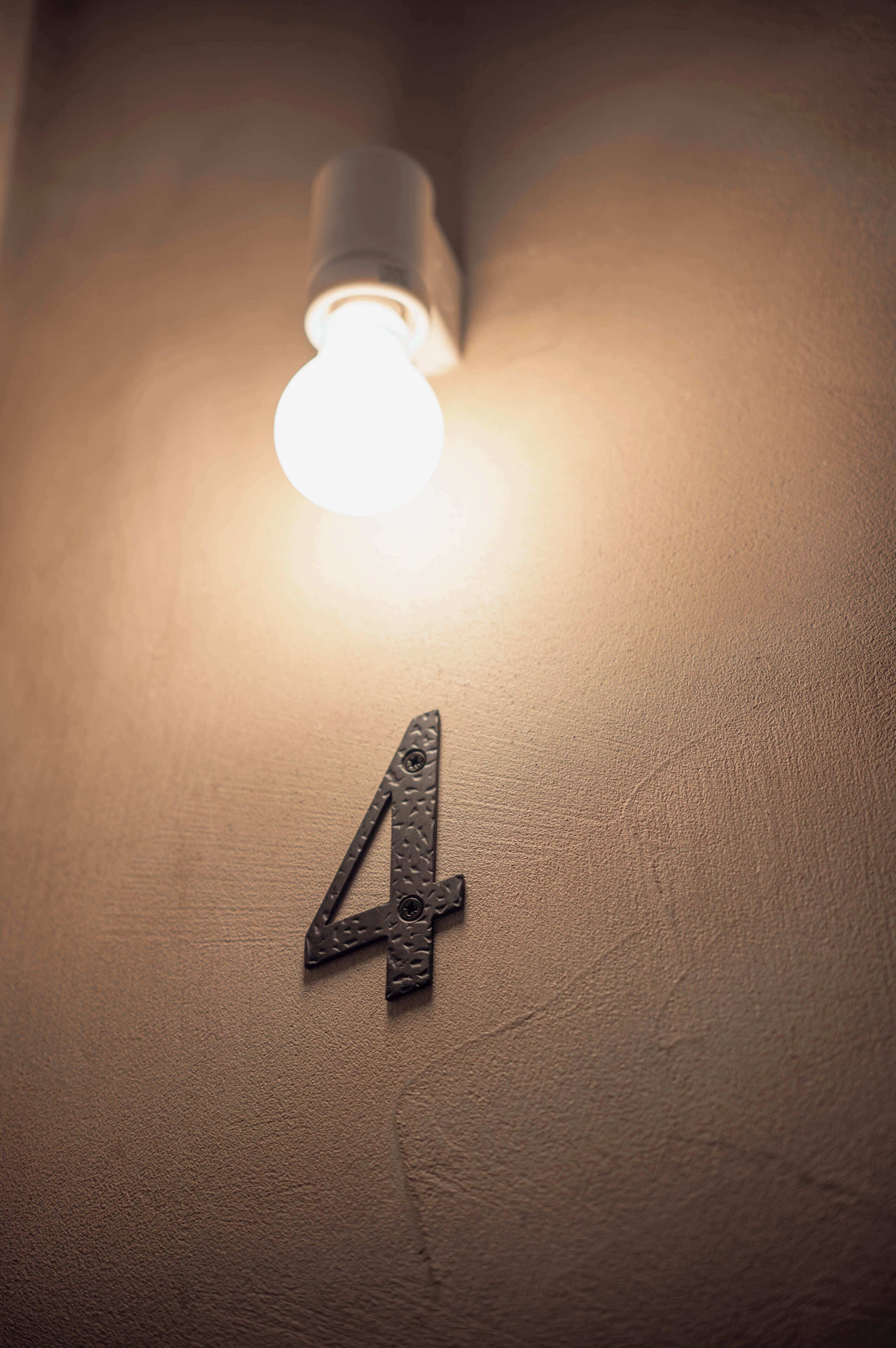 Primer plano de una pared texturizada con una lámpara y el número metálico '4' fijado a ella.