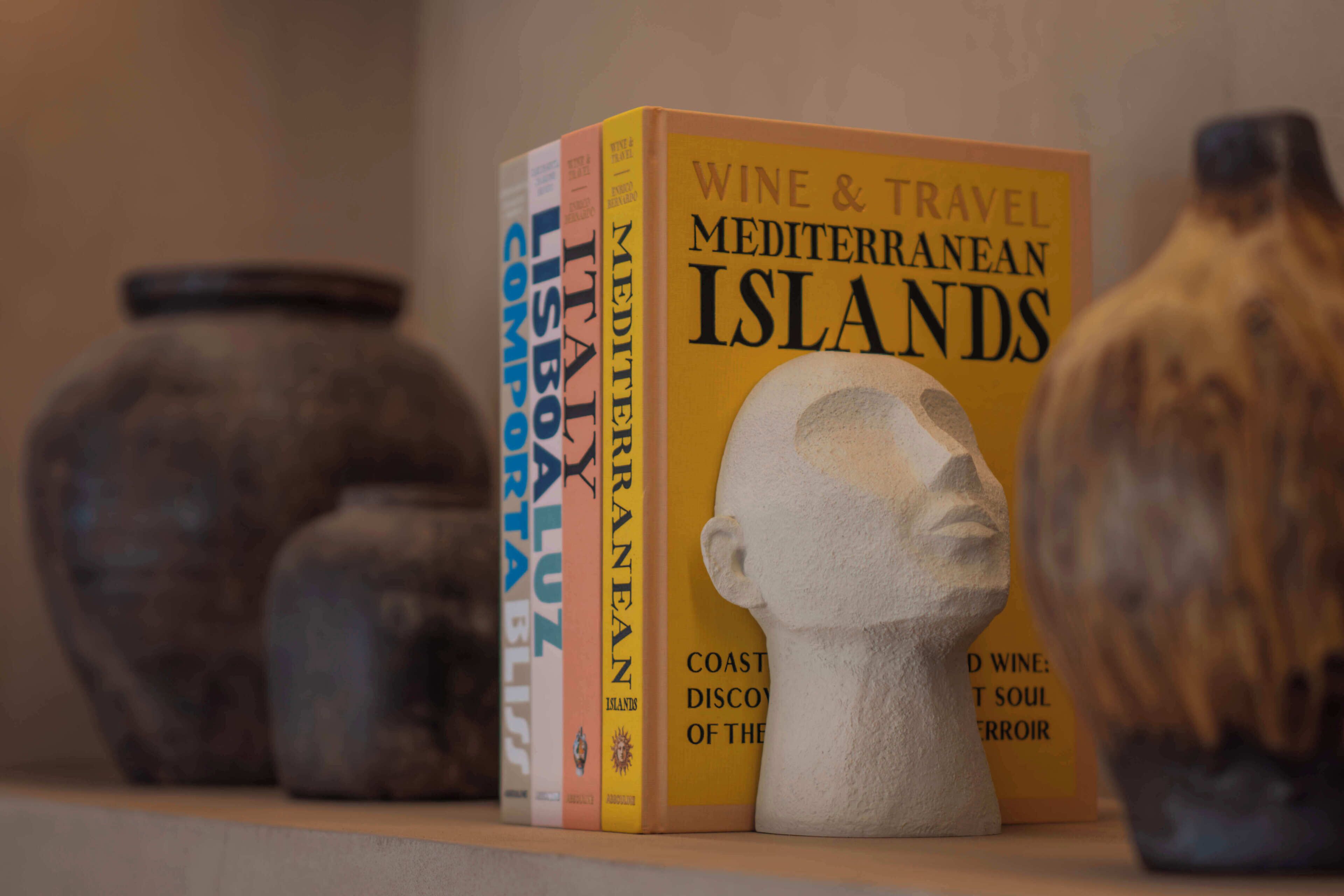 Een boek met de titel 'Wine & Travel Mediterranean Islands' op een plank, samen met decoratieve vazen.