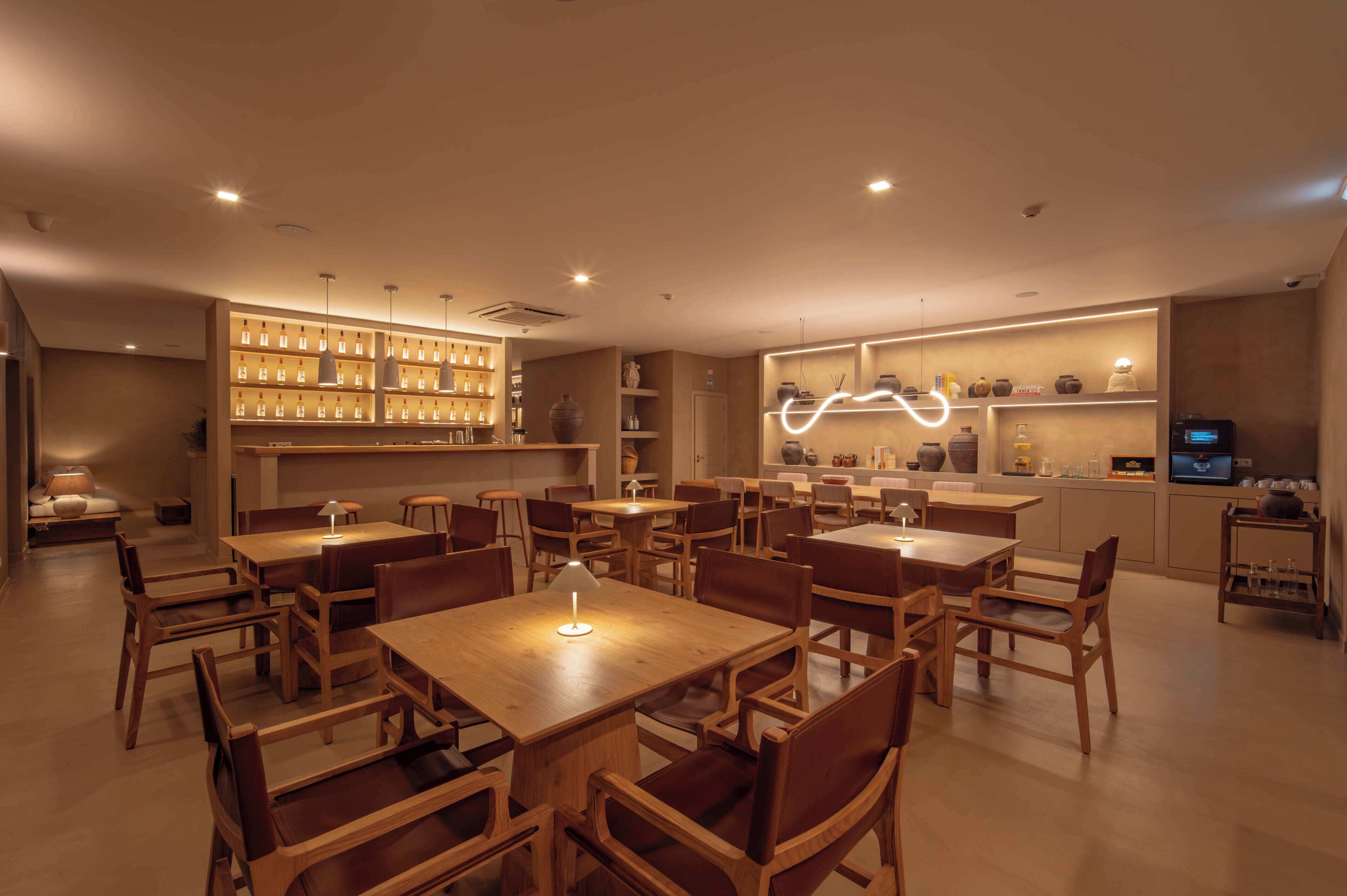 Un restaurante con mesas y sillas de madera, una zona de bar y estantes con botellas.