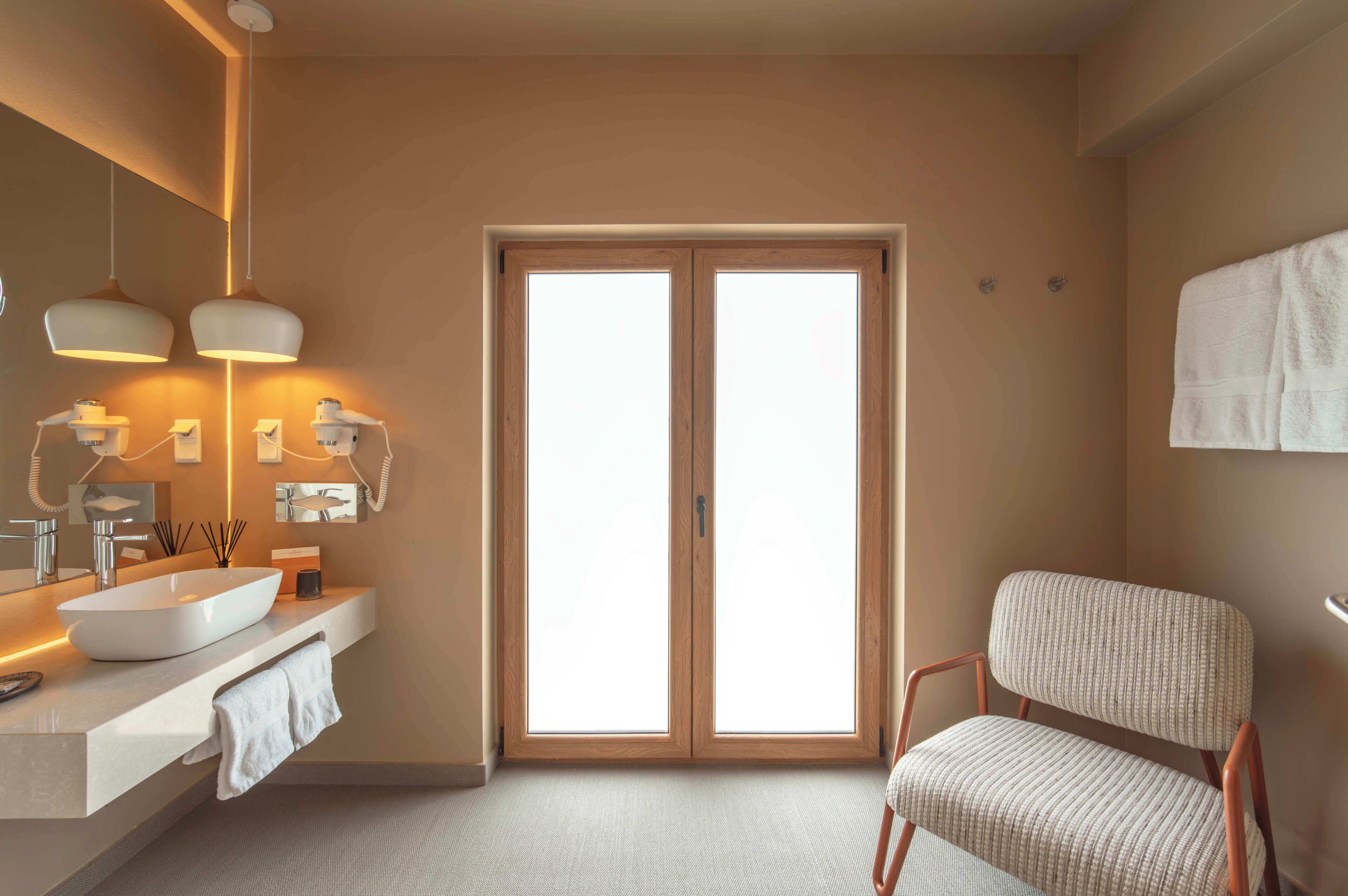 Een moderne badkamer met een grote spiegel, twee hanglampen, een witte wastafel en een houten deur.