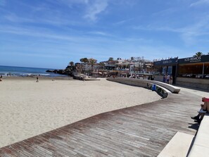 Ein Strand mit einer Holzpromenade, Geschäften und einem Restaurant namens 'Los Remos'.