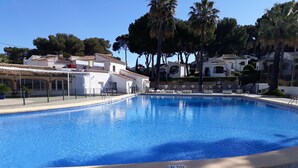 A clear swimming pool with a tiled deck, surrounded by white buildings and palm trees. - Love 2 bed apartment.  Sleeps 4 with wifi, satellite TV and pool. (Xàbia)