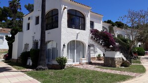 A white building with arched windows and a stone base, surrounded by a well-maintained lawn and a paved walkway. - Love 2 bed apartment.  Sleeps 4 with wifi, satellite TV and pool. (Xàbia)