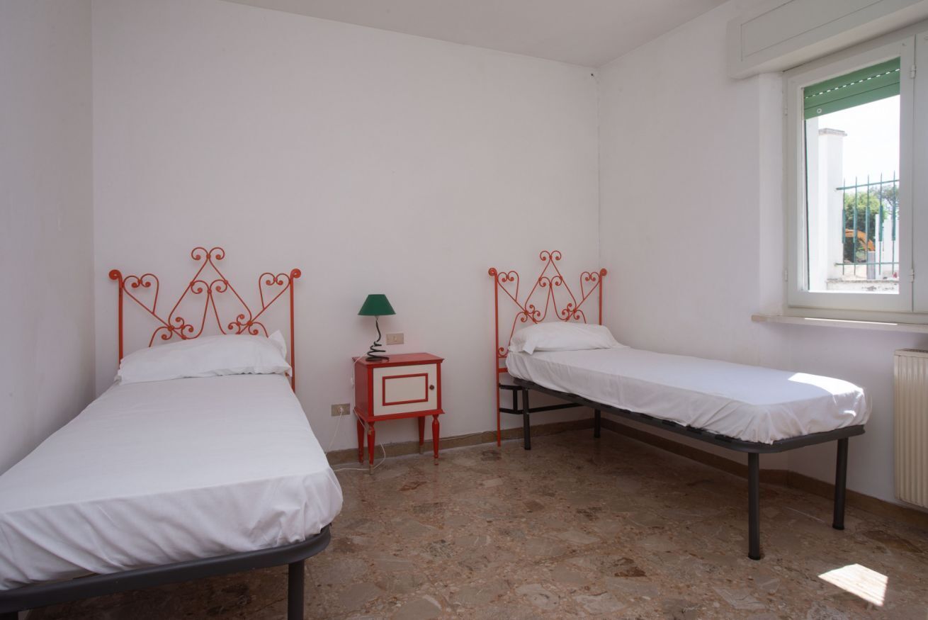 A room with two single beds, a small table with a lamp, and a window with a view.