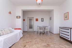 A room with a bed, a dining table with chairs, a cabinet, and a door leading to another room.
