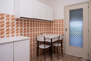 A small kitchen with a white table and chairs, a white cabinet, and a patterned backsplash.