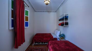 Un dormitorio con dos camas, un armario, estante con ropa, lámpara colgante y una alfombra estampada.