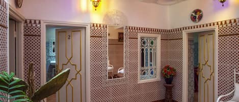 A hallway with patterned walls, a potted plant, and a mirror.