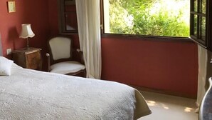 Une chambre avec un grand lit, une chaise, une table de chevet et une fenêtre donnant sur un paysage verdoyant.