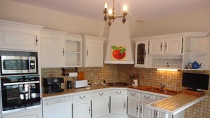 Une cuisine avec des meubles blancs, un four à micro-ondes, une cuisinière, un évier et un lustre.