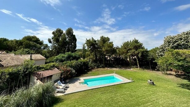 Un jardin à l’arrière de la maison, avec une piscine, entouré d’arbres et doté d’une pelouse bien entretenue.