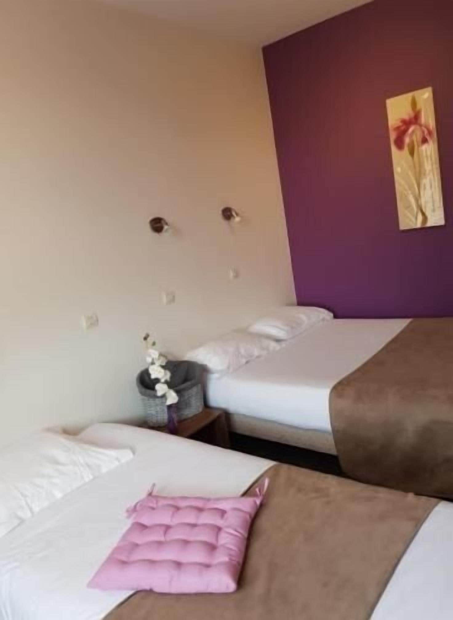 A hotel room with two beds, a purple accent wall, and a small decorative item on the nightstand.