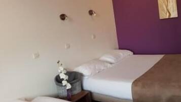 A hotel room with two beds, a purple accent wall, and a small decorative item on the nightstand.