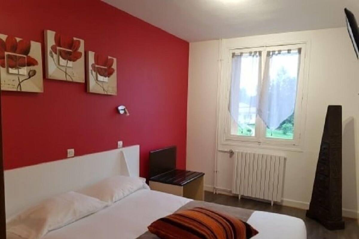 A bedroom with a bed, a window with curtains, a radiator, and a wall with framed pictures.