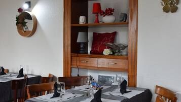 A dining area with wooden tables and chairs, a wooden cabinet with shelves, and a mirror on the wall.