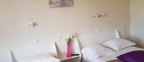 A hotel room with two single beds, a nightstand, a wall-mounted light, and a decorative wall piece.