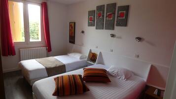 A hotel room with two beds, a window with red curtains, a radiator, and wall art.