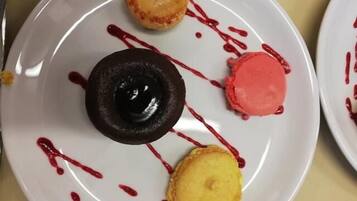 A dessert plate with various items including a chocolate dessert, a pink macaron, and a yellow pastry, all drizzled with red sauce.