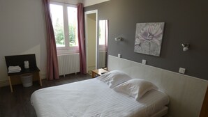 Una cama bien hecha con sábanas blancas en una habitación con un ventanal grande, un radiador y un cuadro en la pared.