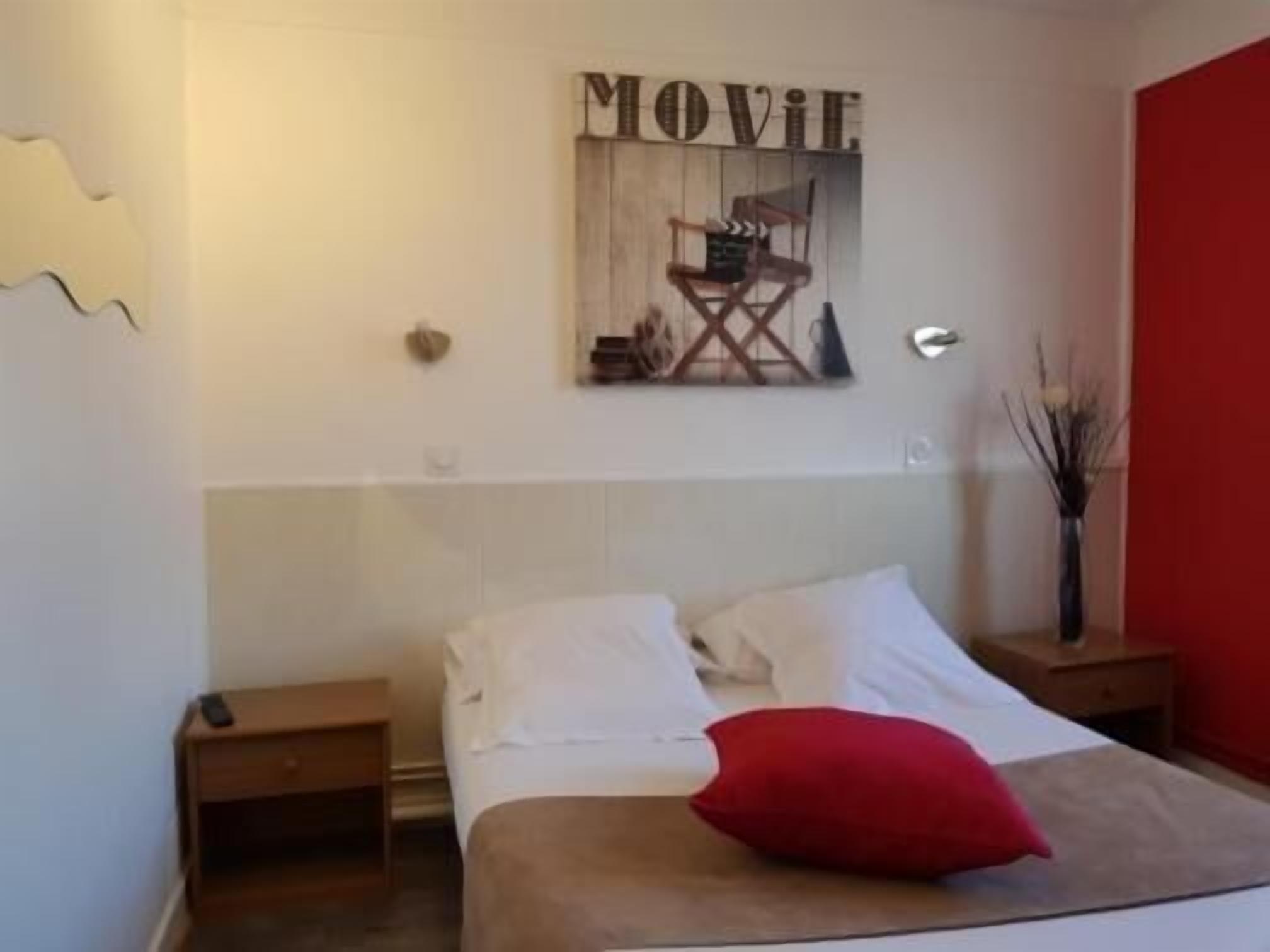 A bedroom with a bed, a nightstand, a red pillow, a wall-mounted movie sign, and a red wall.