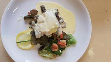 Un plato blanco con un guiso de pescado, una rodaja de limón y vegetales verdes.