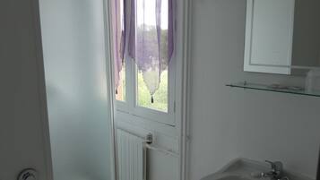 A bathroom with a toilet, a sink, a window with purple curtains, and a mirror.