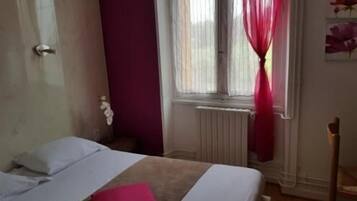 Una habitación de hotel con cama, ventana con cortinas, radiador y una silla.