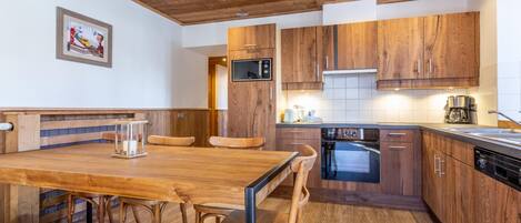 Una cocina moderna con armarios de madera, horno integrado y comedor con mesa y sillas de madera.