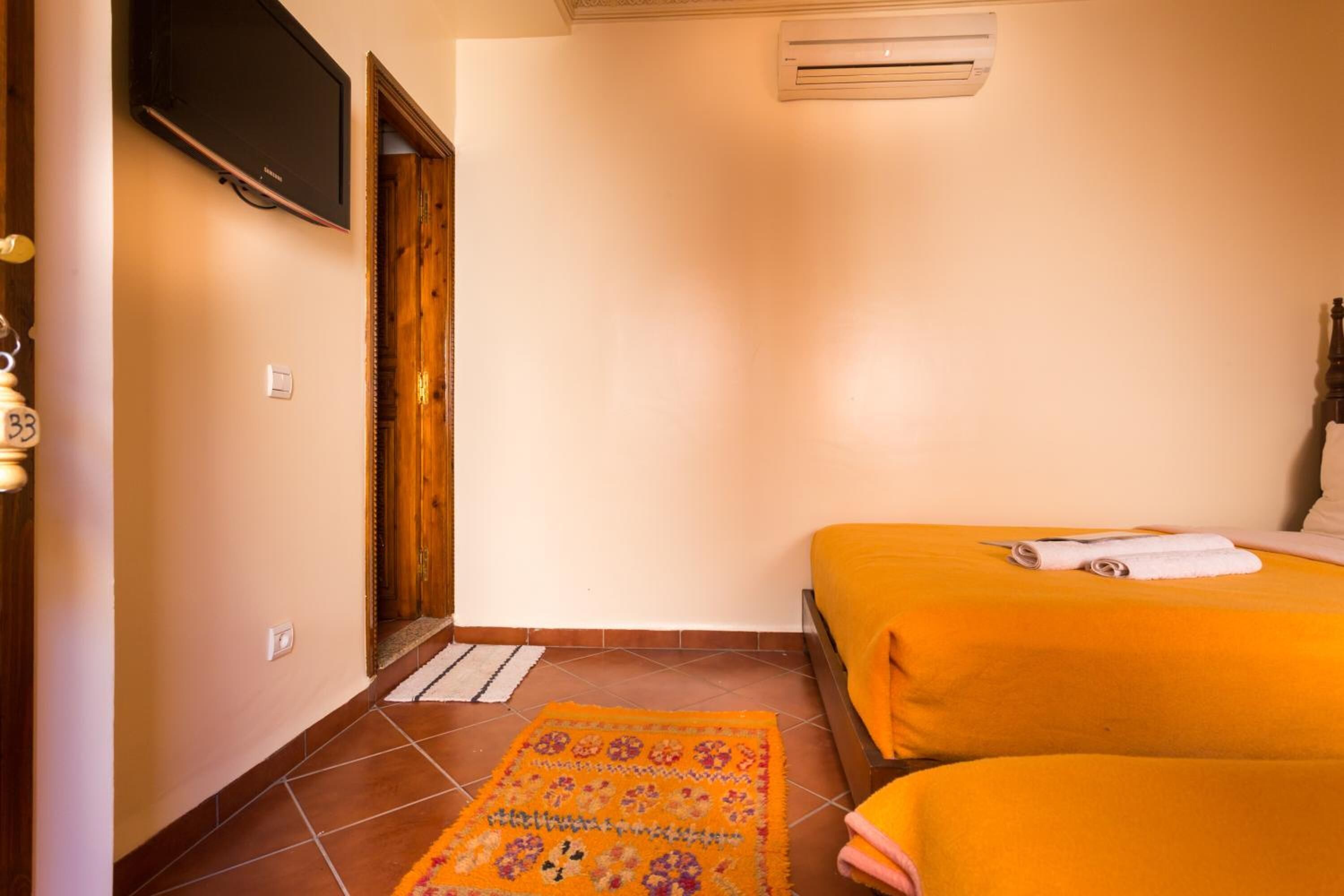 Quarto de hotel com duas camas, televisão, ar condicionado e um tapete estampado.