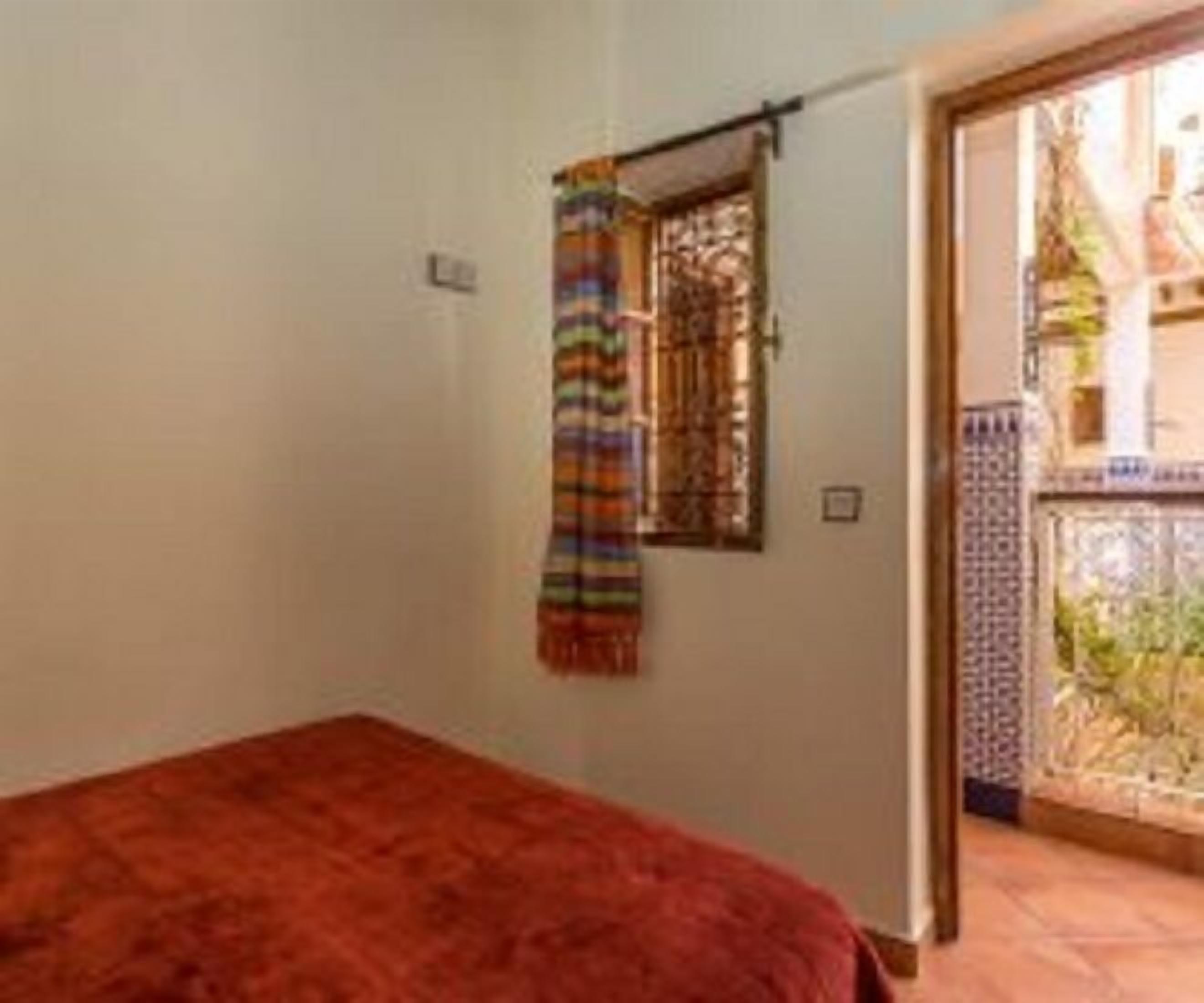 Una habitación con una cama, un ventanal con cortina y una puerta que da a un espacio exterior.