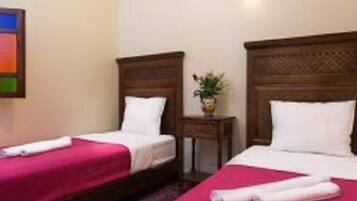 Une chambre d’hôtel avec deux lits simples, chacun doté d’une tête de lit en bois, d’une petite table de chevet avec une plante et d’une couverture rouge.