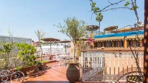 Un patio en la azotea con mesas al aire libre, plantas en macetas y una valla decorativa.