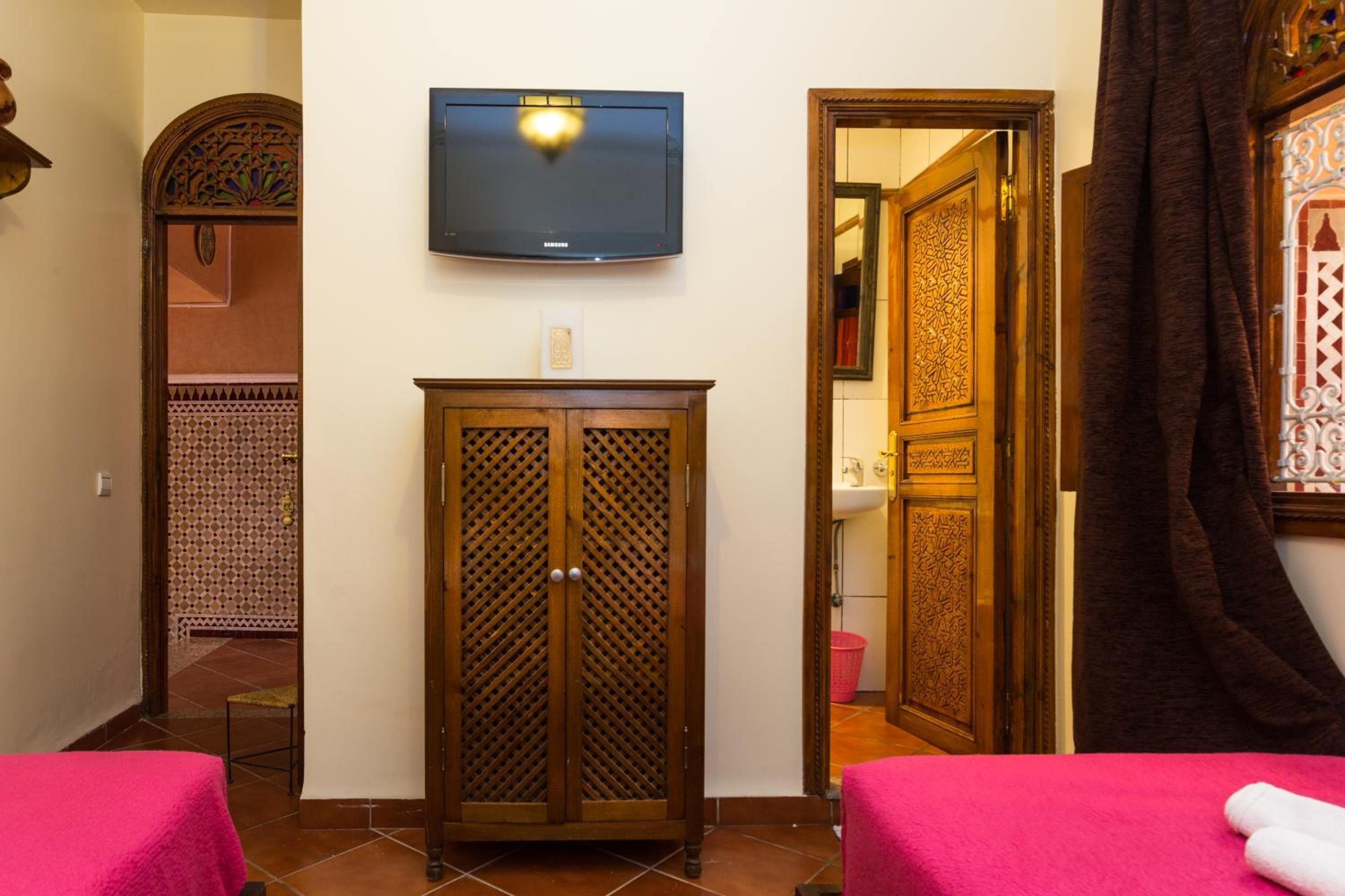 A hotel room with two beds, a television mounted on the wall, and a wooden wardrobe.