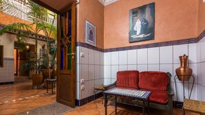 Un vestíbulo con un sofá rojo, una mesa estampada y una pared con azulejos que presenta un cuadro.