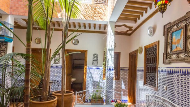 Un patio con macetas, un banco de metal y paredes con azulejos.
