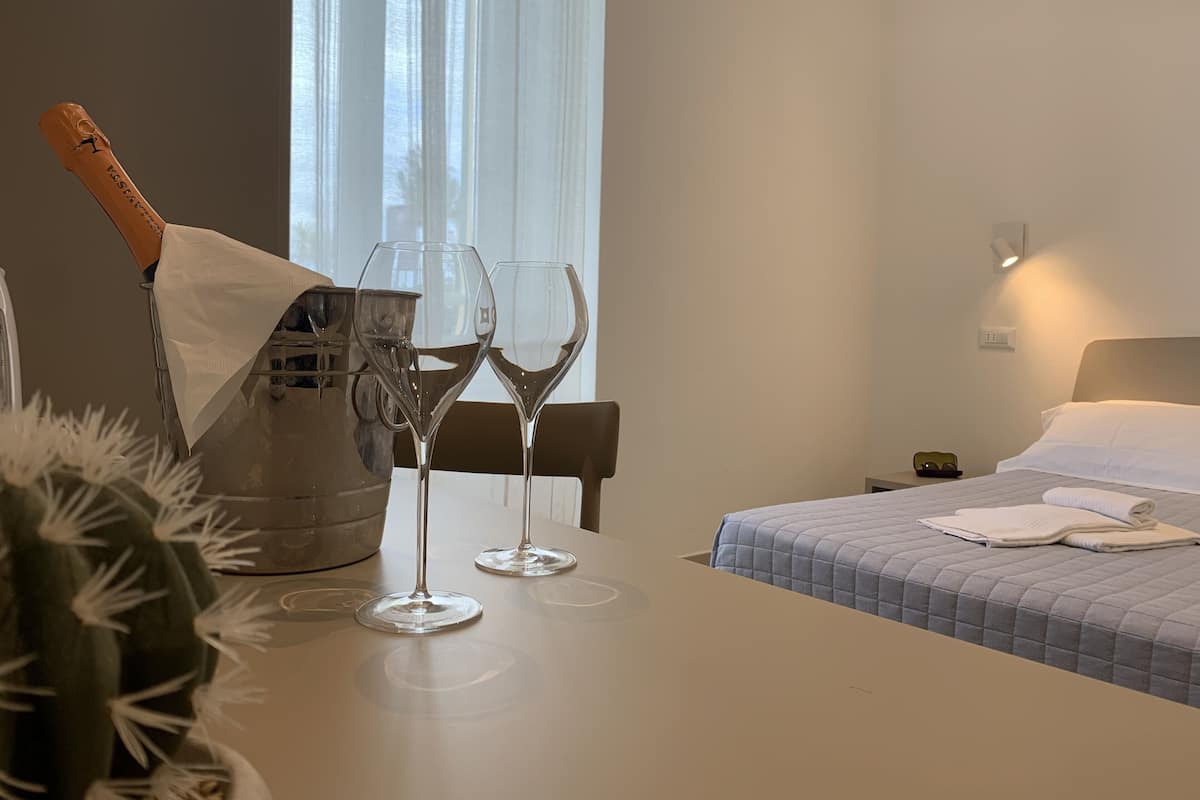 Habitación de hotel con una cama, una mesita de noche con dos copas de vino y una botella de champán, además de una planta de cactus.